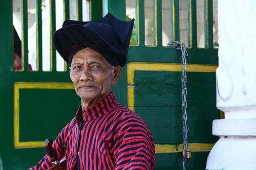 Free Elderly man wearing traditional attire stands near a green and yellow door outdoors. Stock Photo