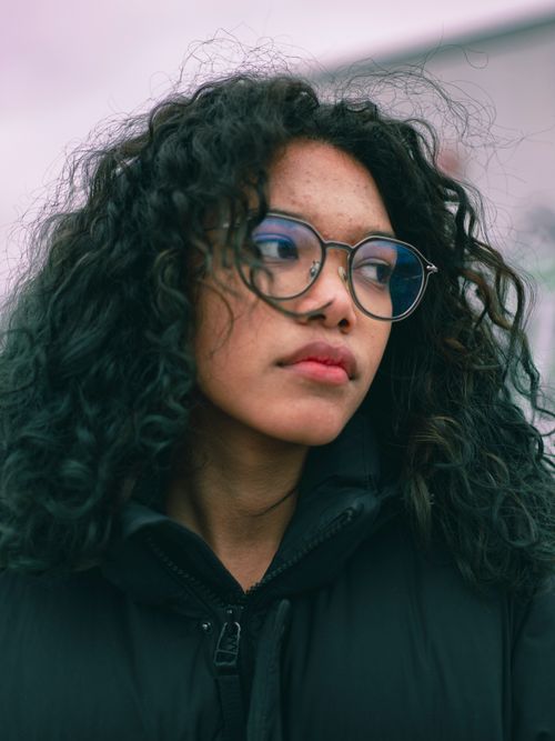 Free Portrait of a young woman with curly hair wearing eyeglasses, captured outdoors in Toronto, Canada. Stock Photo