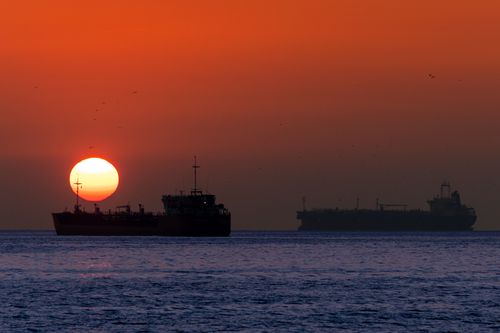 Free Dramatic ocean sunset with silhouetted ships creates a serene seascape view. Stock Photo