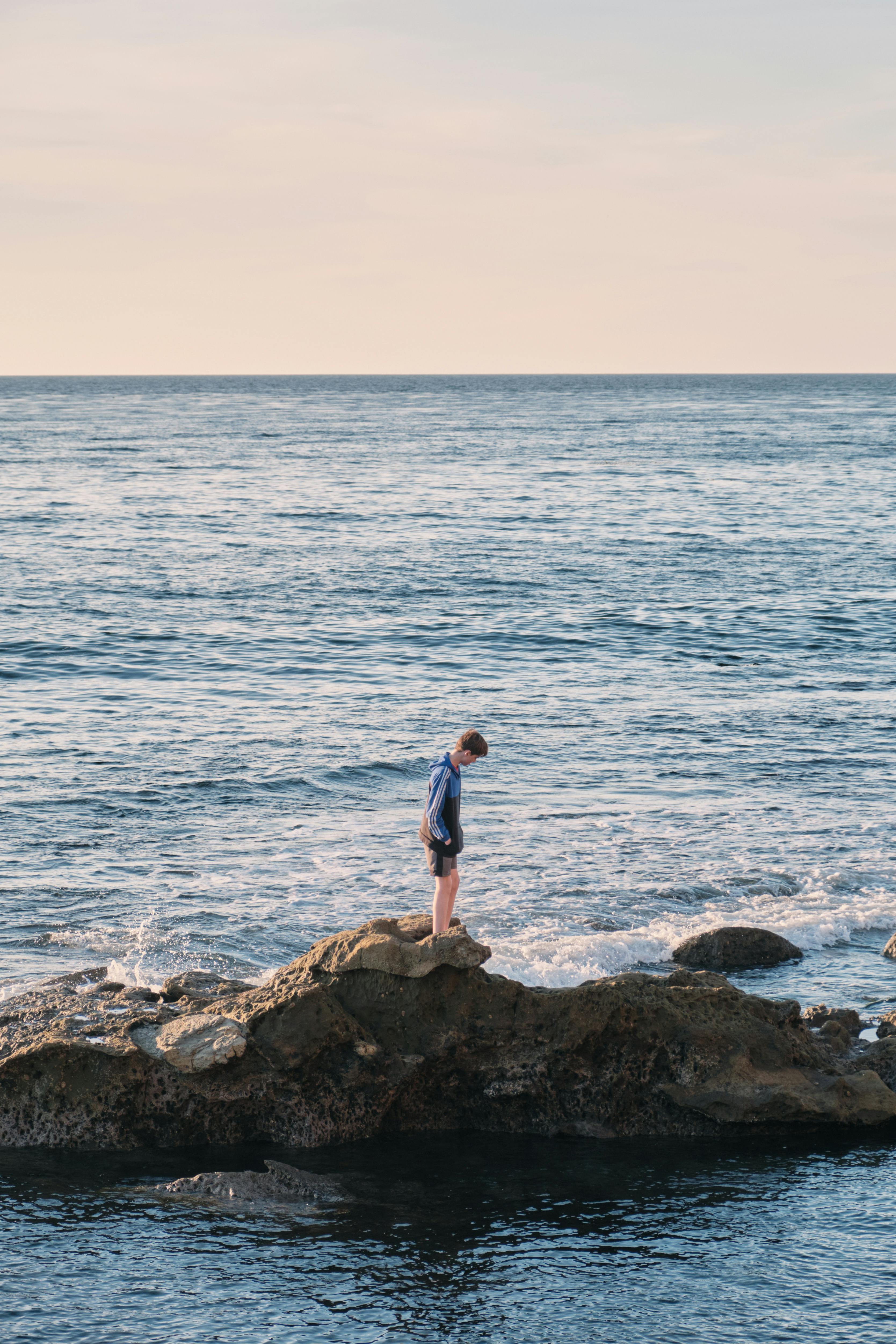 A person stands on rocks gazing at the ocean, embodying solitude and contemplation.
