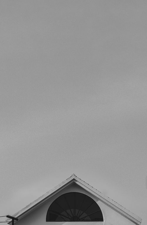 Free A minimalist black and white photo showcasing the geometric rooftop design of a house under a cloudy sky. Stock Photo