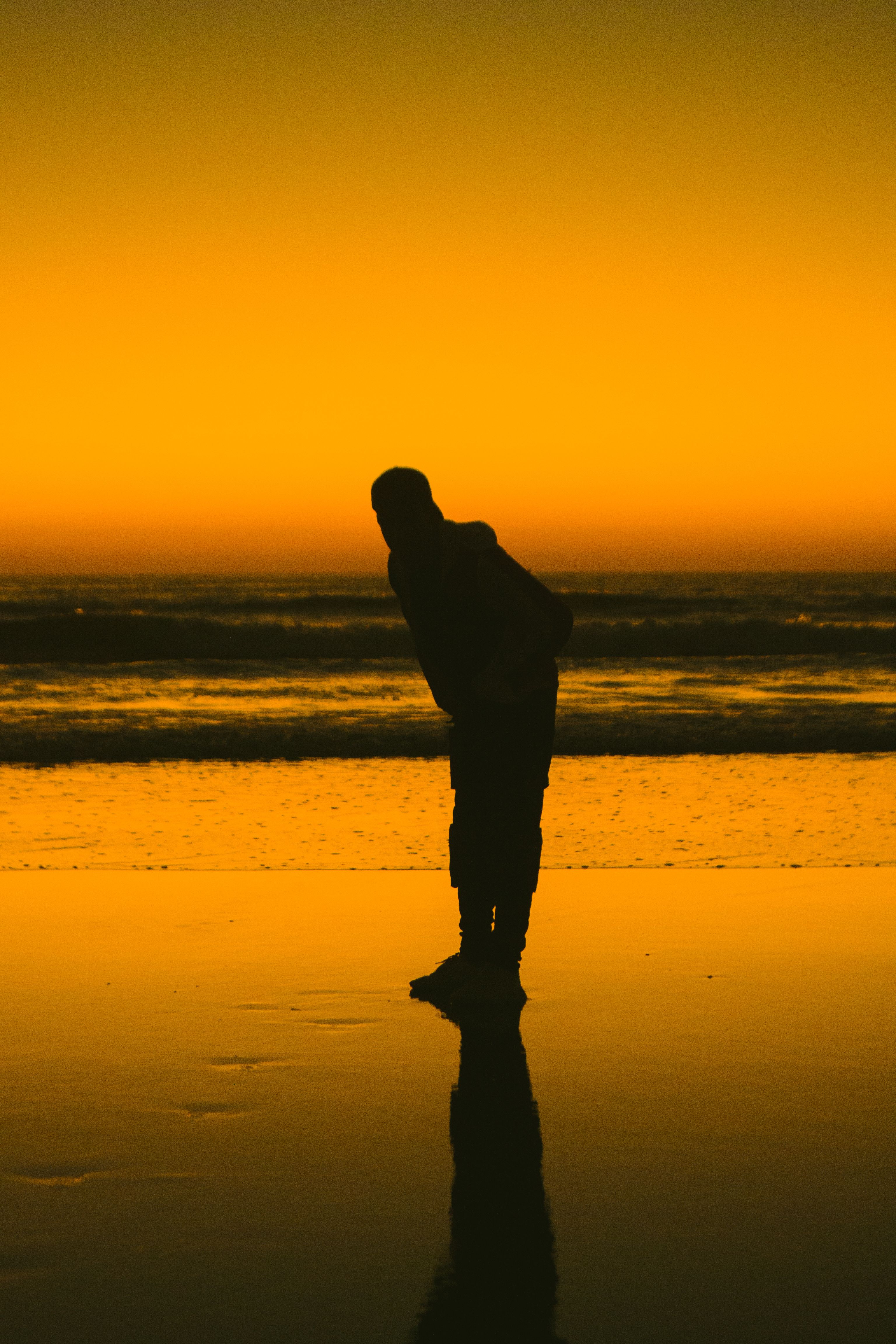 A silhouette of a person standing on the beach at sunset · Free Stock Photo