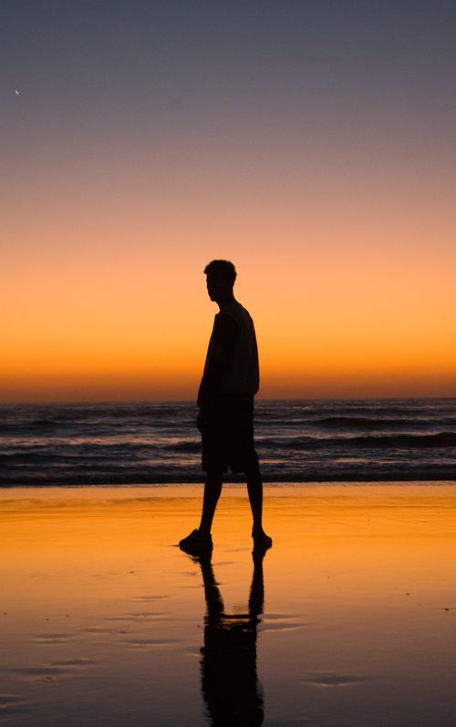 Free A man walks along a Moroccan beach with a stunning sunset in the background, creating a peaceful seaside silhouette. Stock Photo