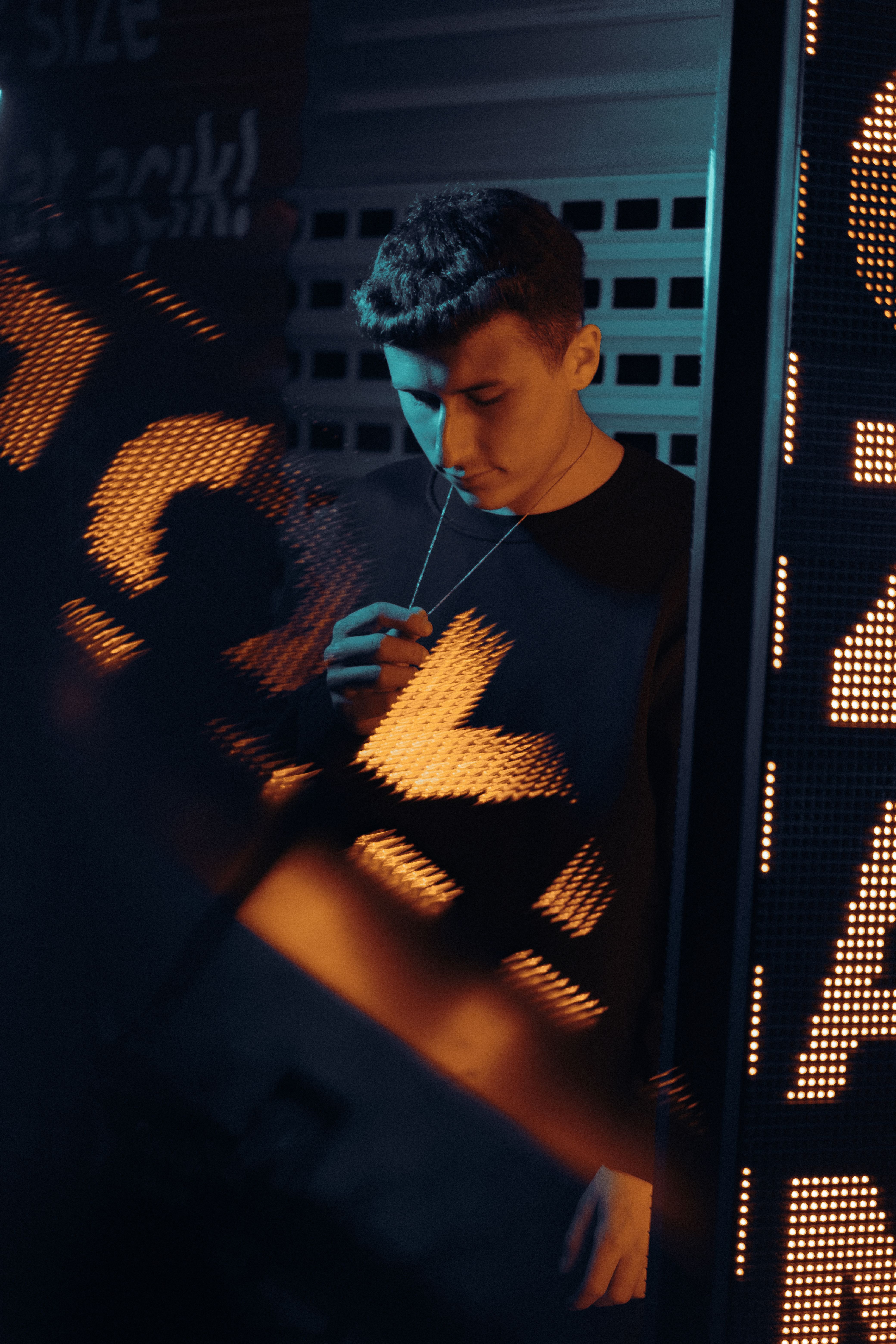 Man holding a necklace in moody neon light setting.