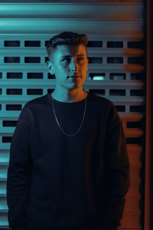 Free A young man in a black sweater looking upwards, illuminated by ambient lighting, creating a moody atmosphere. Stock Photo