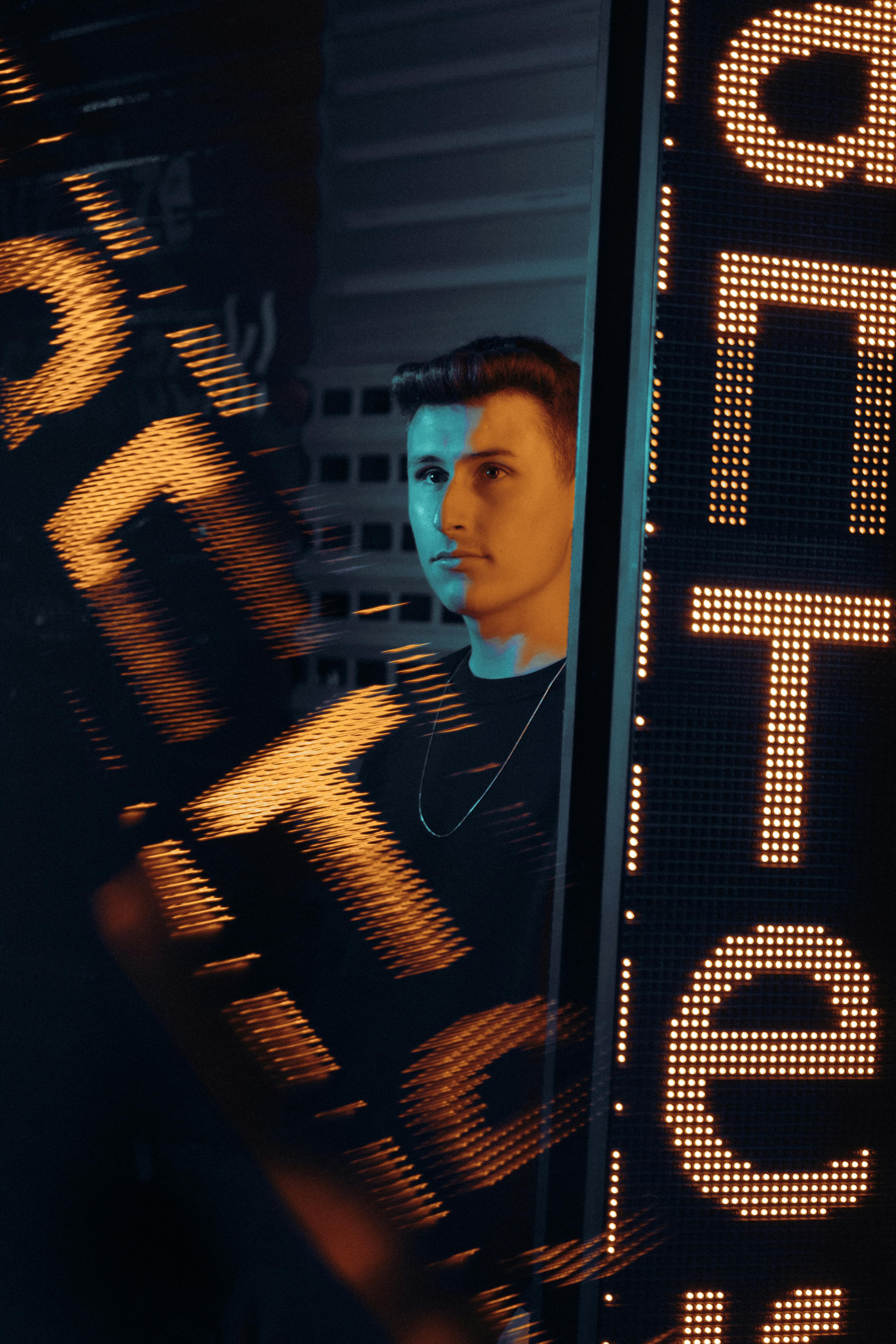 A young man stands by a neon sign, vibrant city night atmosphere.