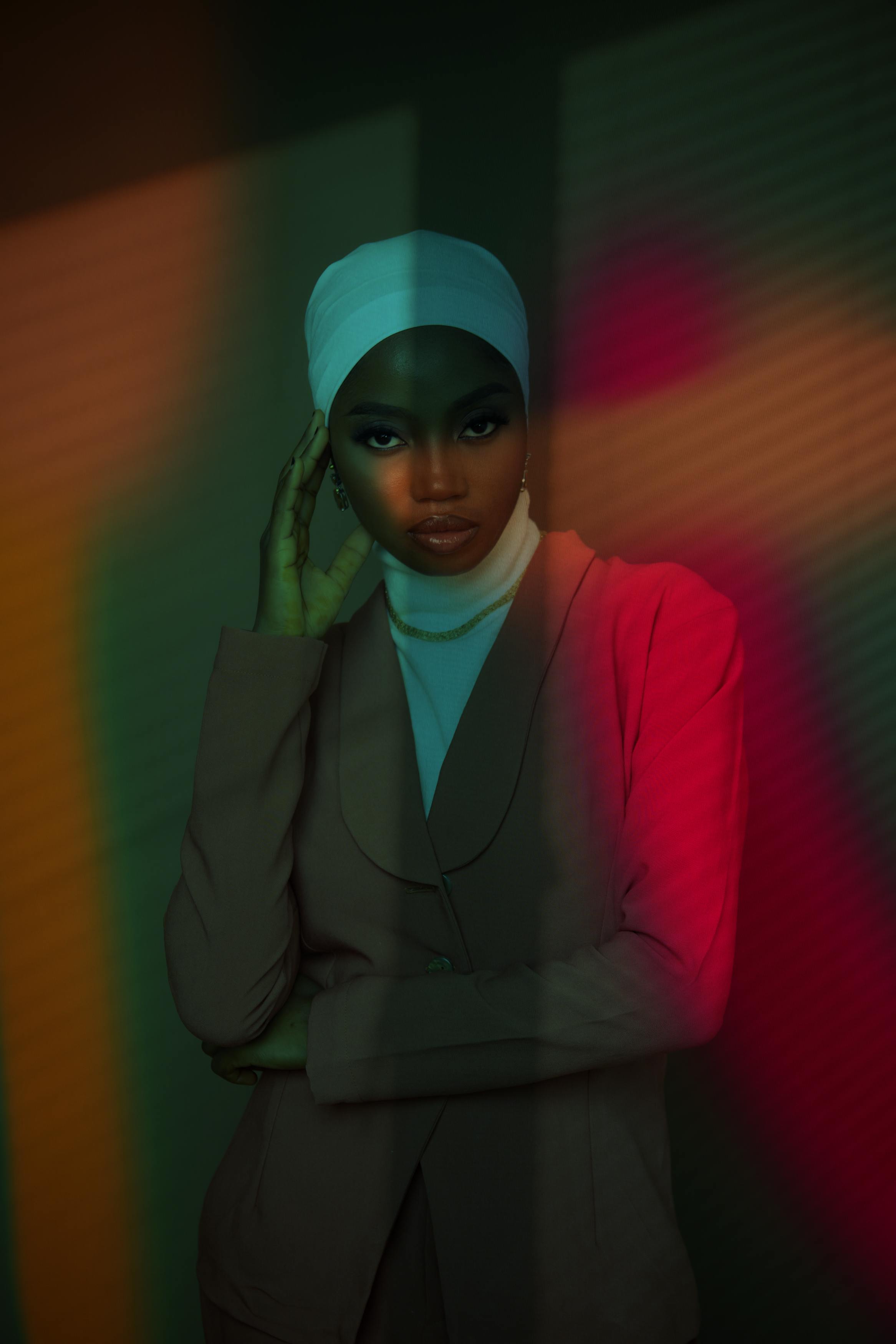 Free Artistic fashion portrait of a woman in a colorful lighting setup wearing a head wrap and blazer. Stock Photo