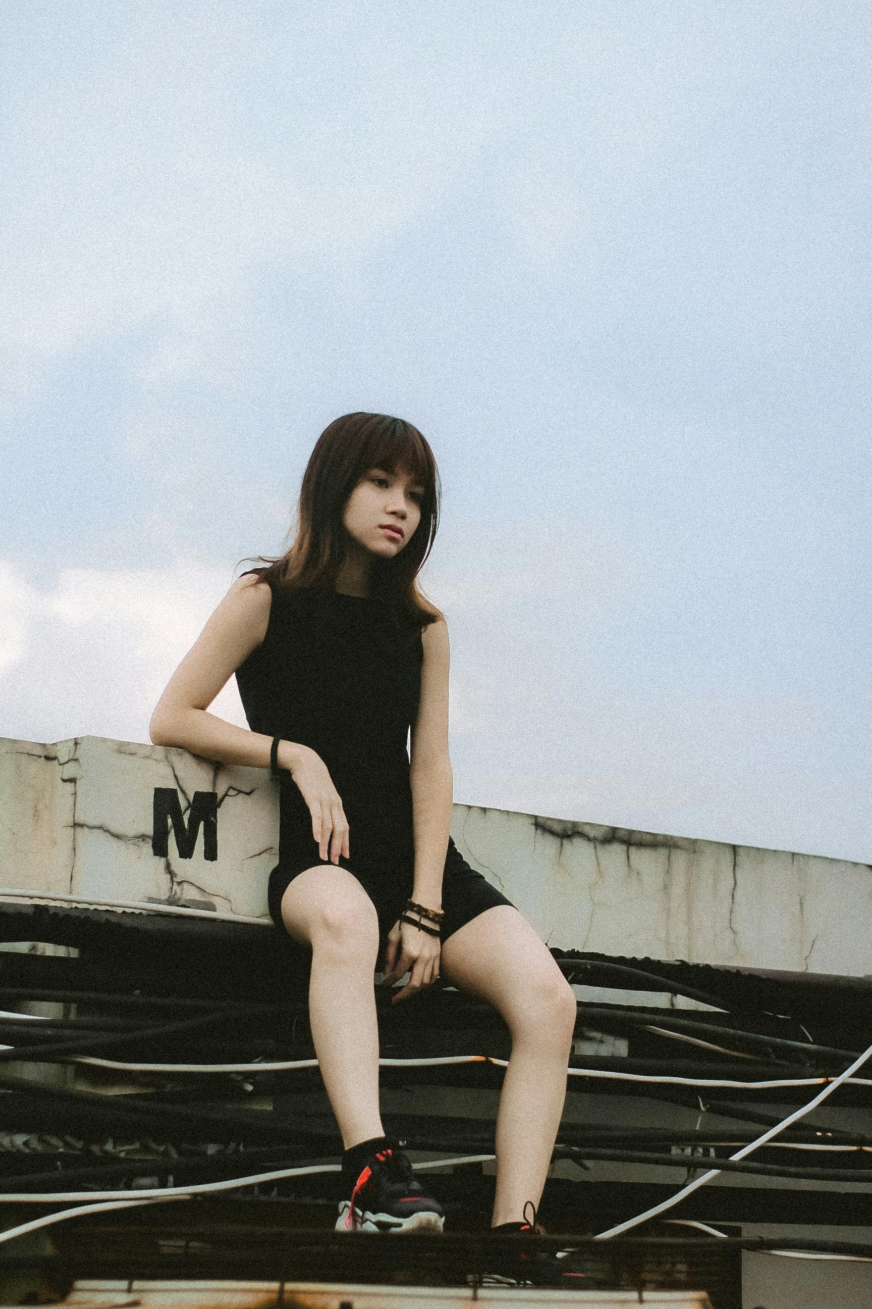 Portrait of a young woman sitting outdoors in Cimahi, Indonesia, against an urban backdrop.