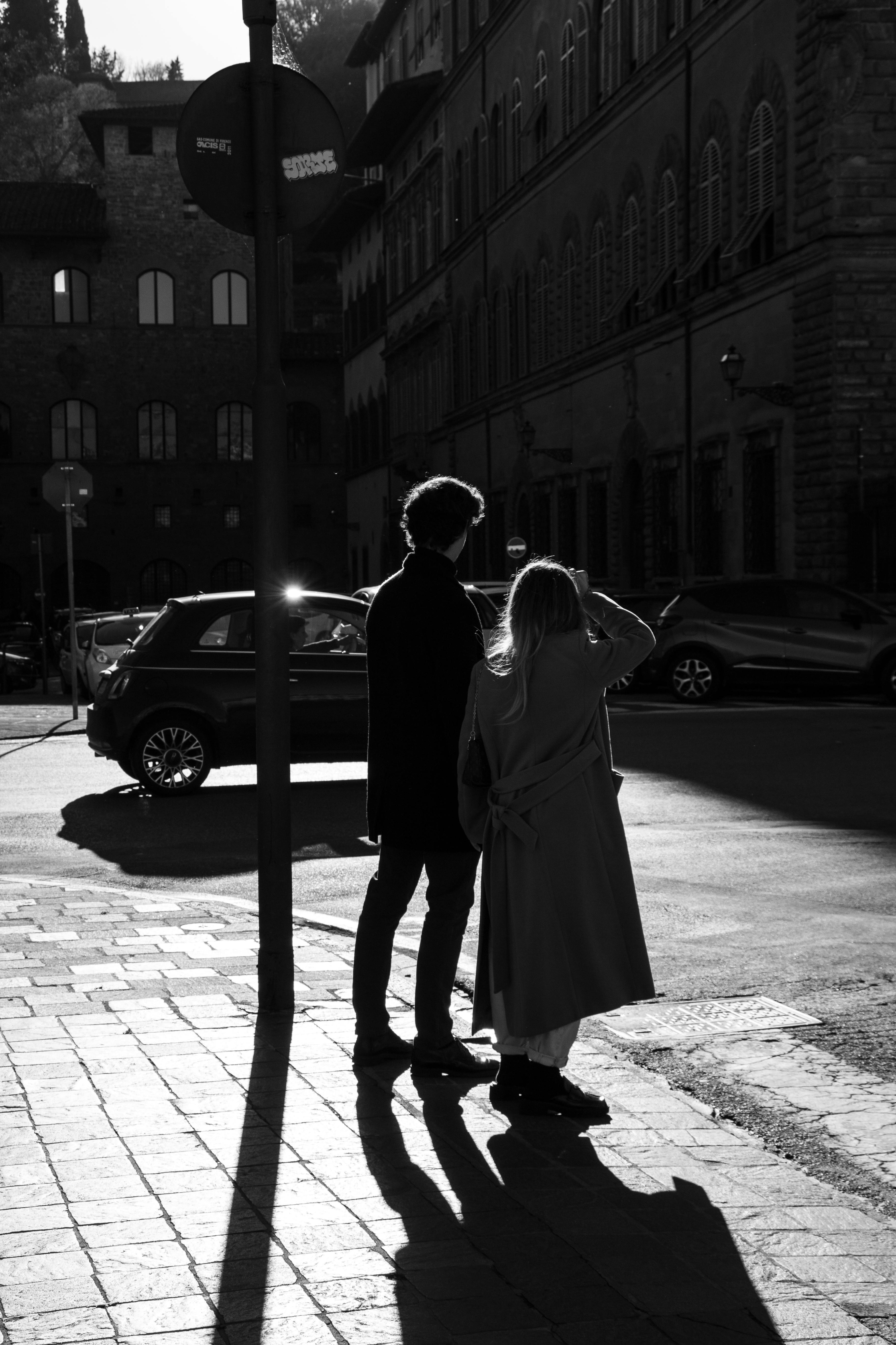 Grayscale image of a couple standing on a street in Tuscany, Italy, capturing urban life.