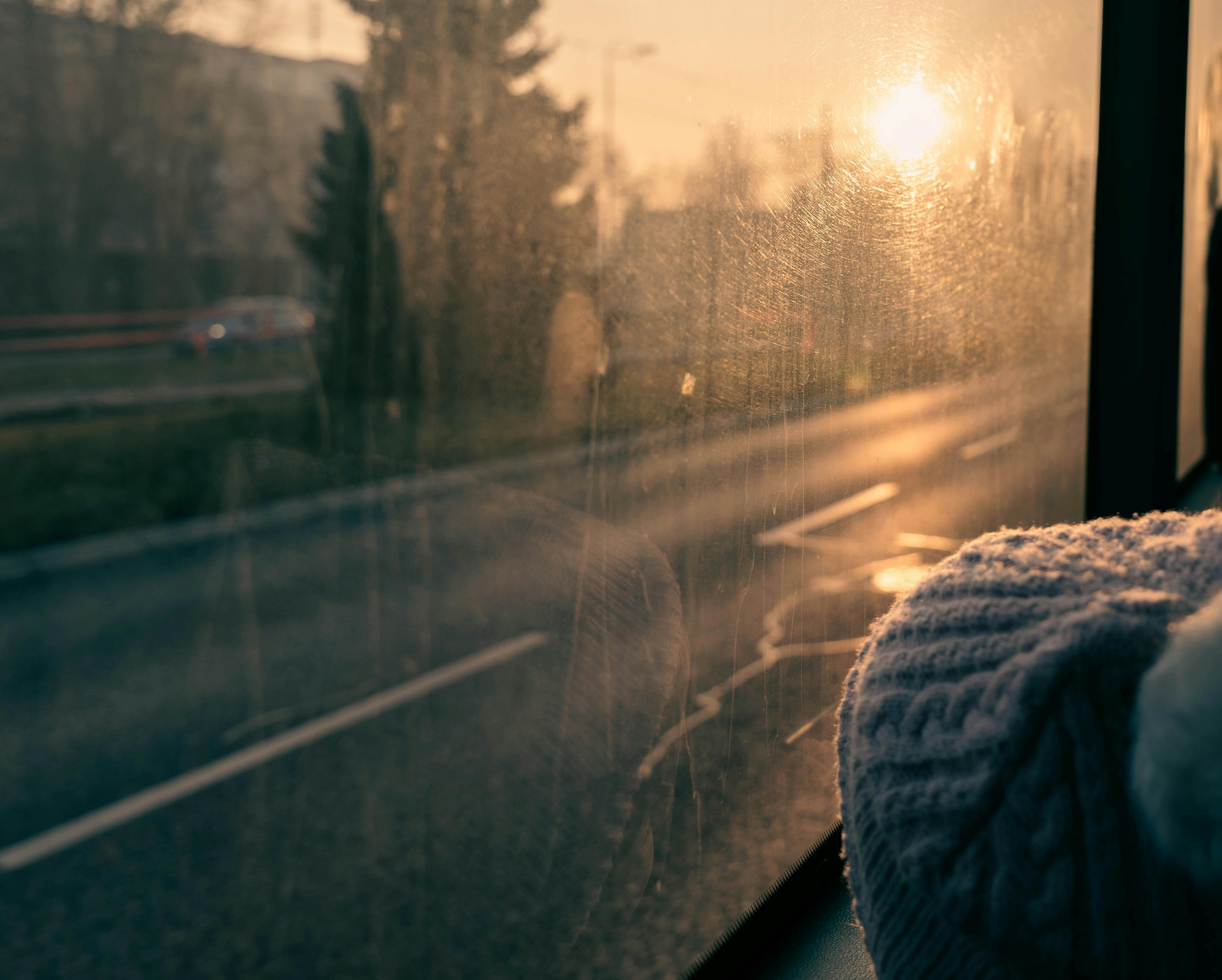 A cozy view of a sunset from inside a bus, highlighting a knitted beanie on the ledge.