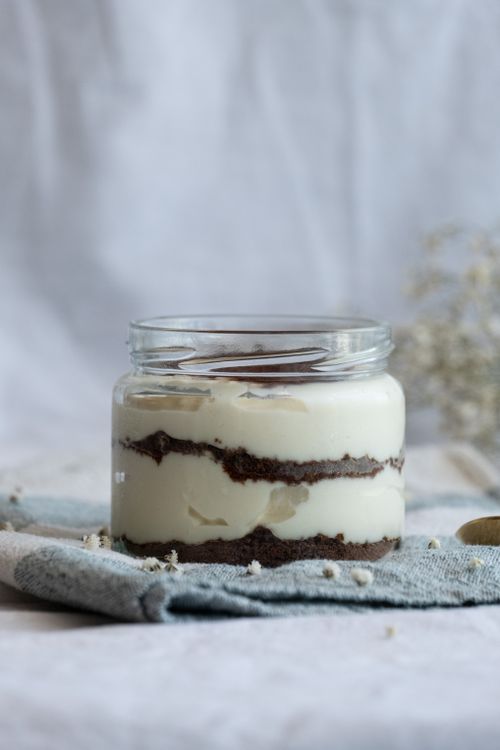 Free Close-up of a creamy tiramisu dessert in a glass jar on a soft fabric background. Stock Photo