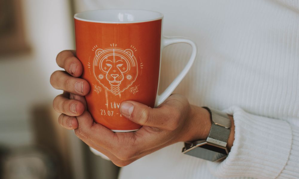 A woman holding a Leo zodiac coffee mug, the morning-coffee moment when most people read their daily horoscope