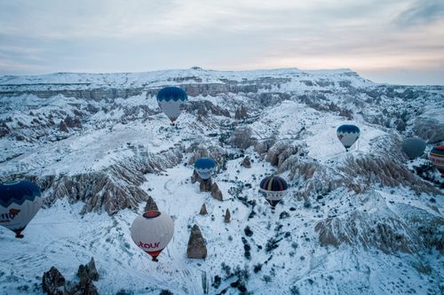 Free Beautiful aerial view of hot air balloons floating over snowy Cappadocia mountains during winter. Stock Photo