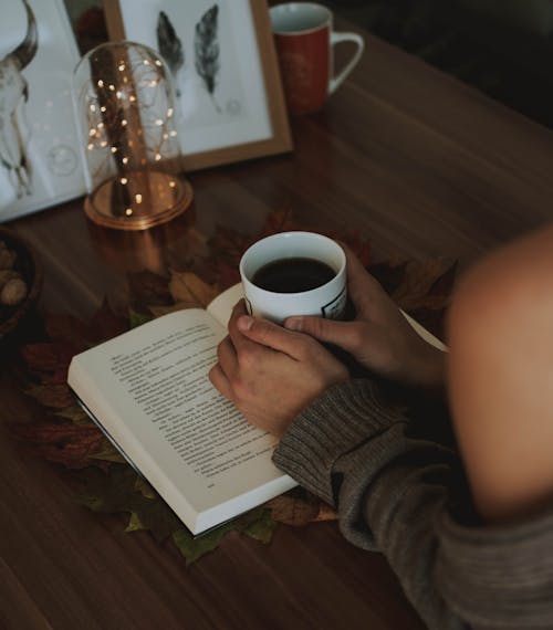 Mädchen Hält Tasse Kaffee über Geöffnetem Buch Auf Braunem Holztisch