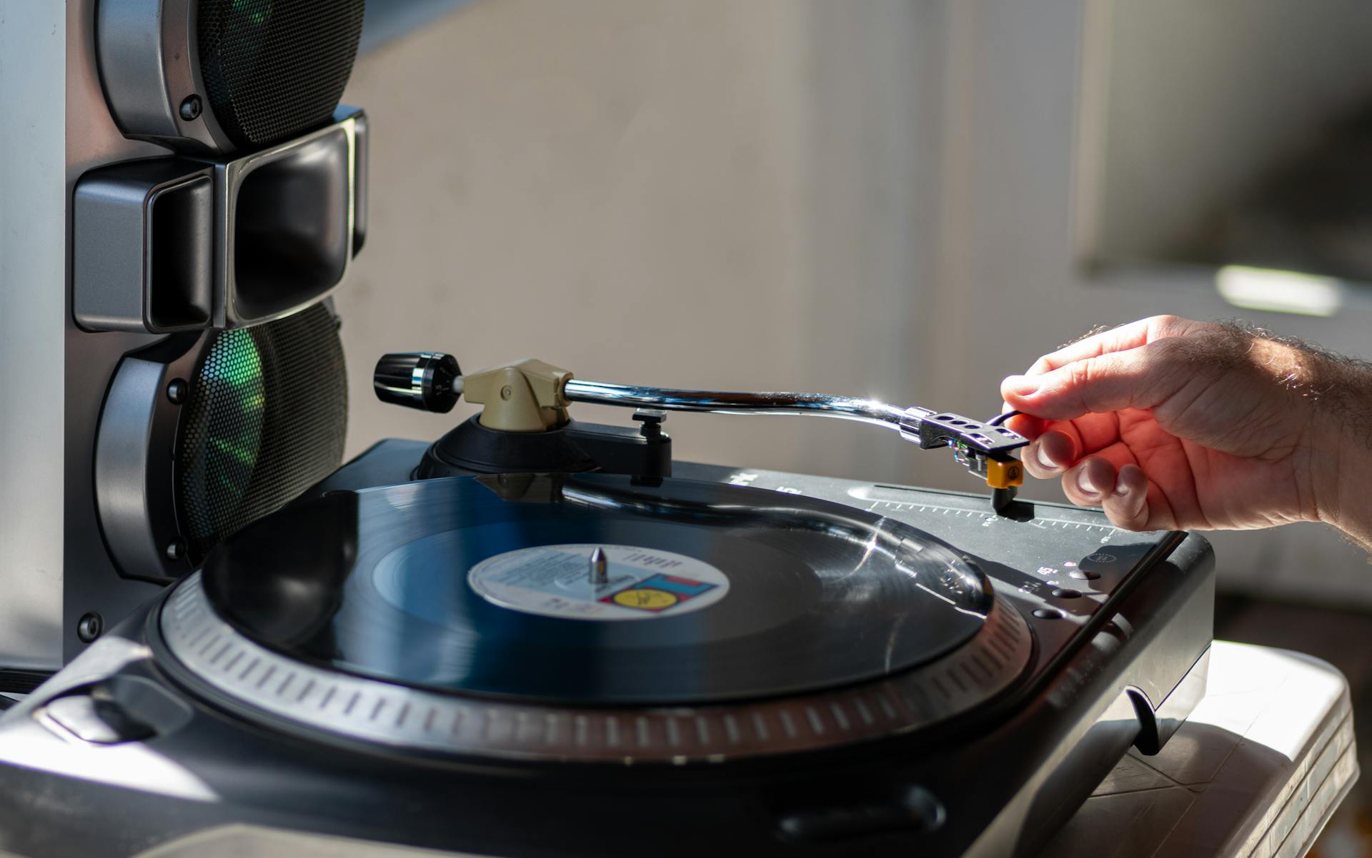 Close-up of a hand adjusting a needle on a vintage vinyl turntable next to speakers.