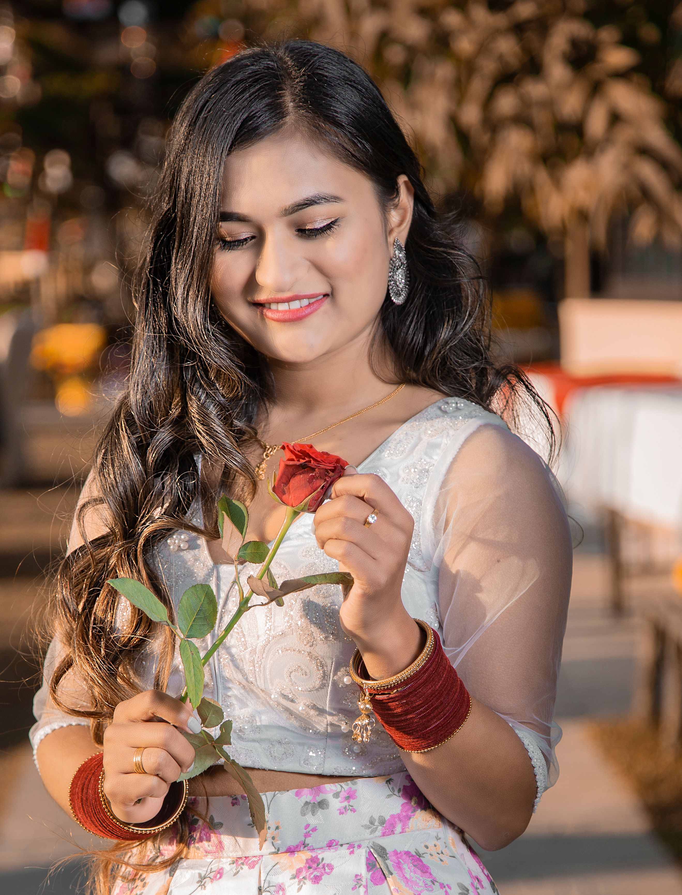 Elegant woman in white dress holding a red rose and smiling outdoors in Pokhara, Nepal.
