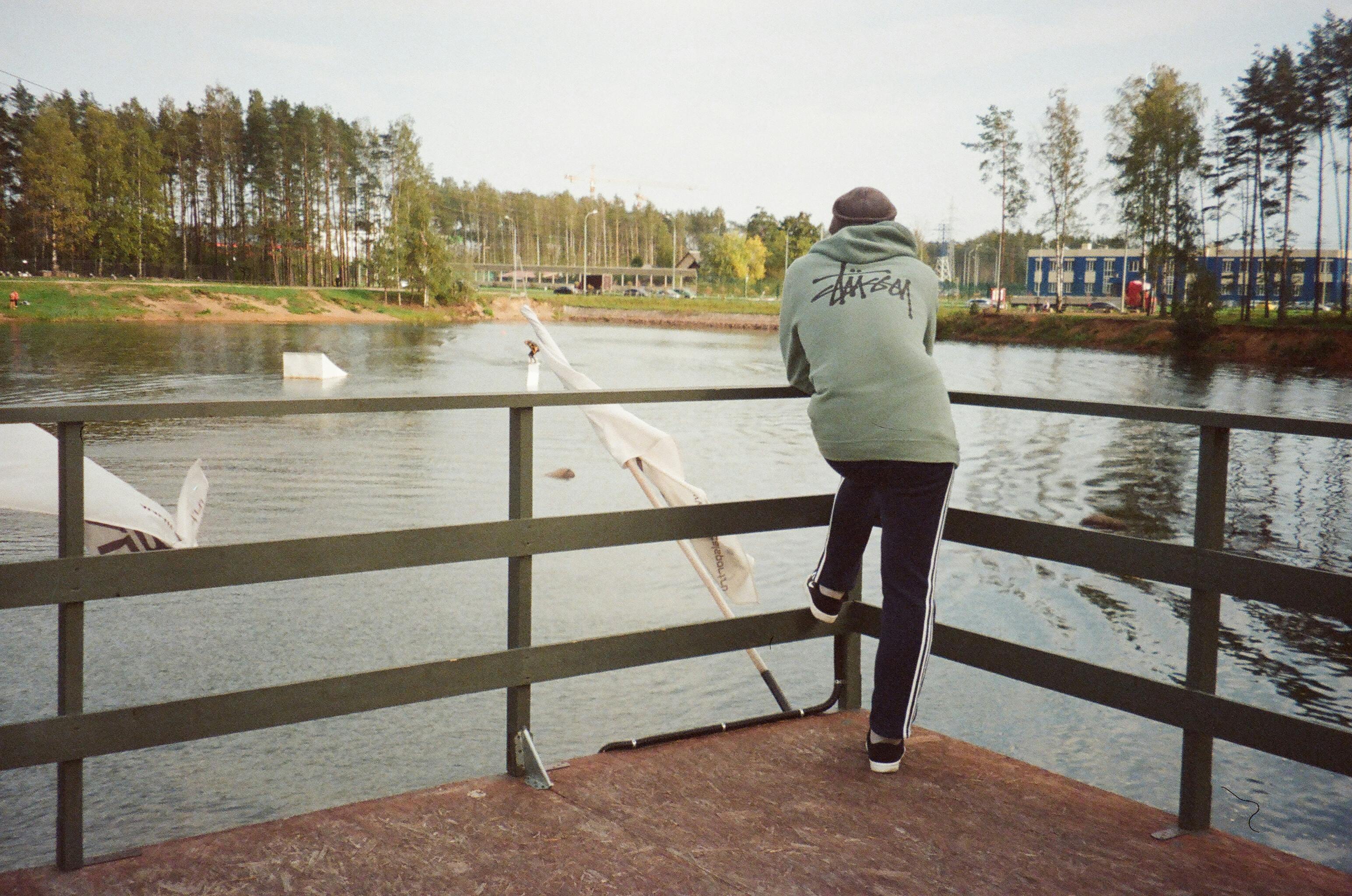 一个穿着连帽衫的人站在湖边，享受着被大自然包围的宁静时刻