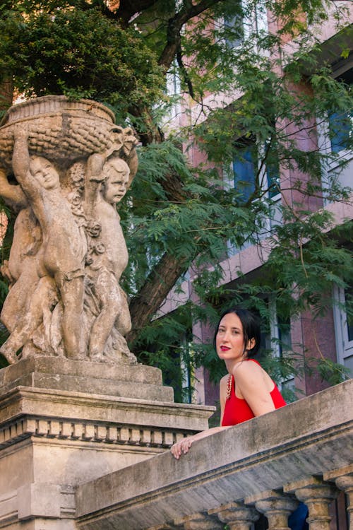 Woman Wearing Red Dress Next to a Classic Sculpture