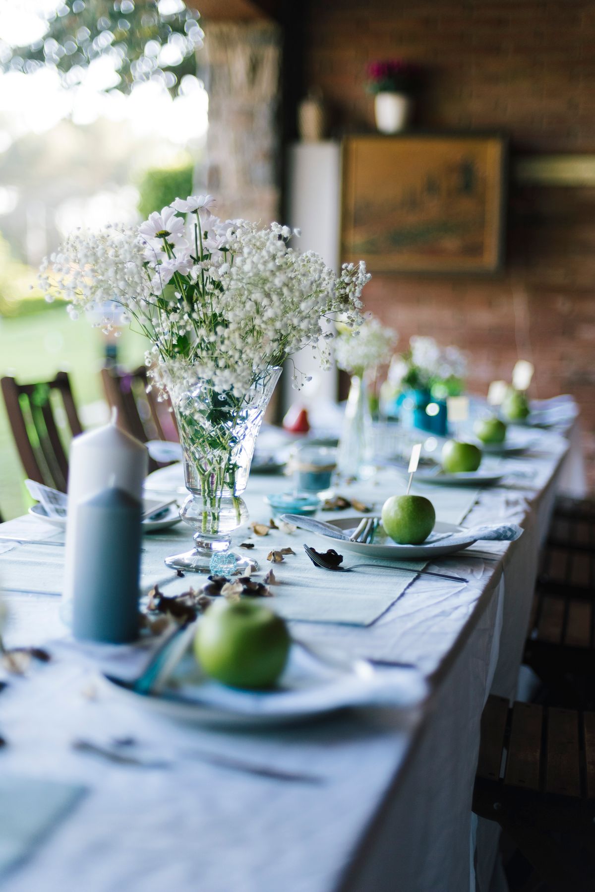 Beautiful table setting with green apples and white flowers in a sunny outdoor setting. Stock Photo.