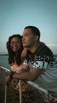 A cheerful couple smiles while enjoying a serene ferry ride during a beautiful day. - Fotografer Sidoarjo