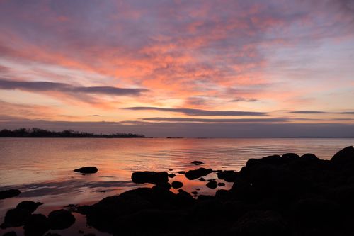 Free Stunning sunset view over a tranquil sea with rocks silhouetted in the foreground. Stock Photo
