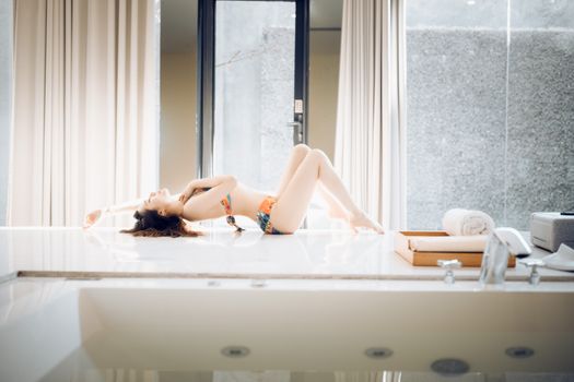 A woman in a swimsuit reclining on a modern bathroom floor, exuding elegance and relaxation.