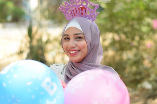 微笑的女人，戴着灰色的盖头头巾，拿着粉色和蓝色的气球