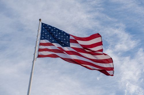 Free A vibrant American flag waves on a pole against a clear, cloudy blue sky, symbolizing patriotism. Stock Photo