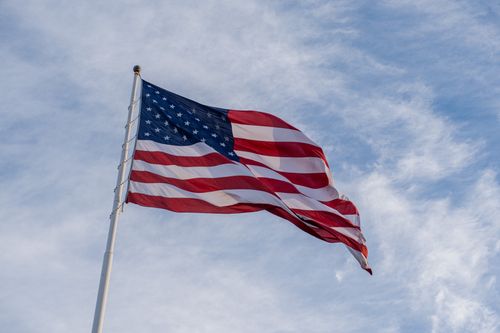 Free A vibrant American flag waving against a clear blue sky, symbolizing patriotism. Stock Photo