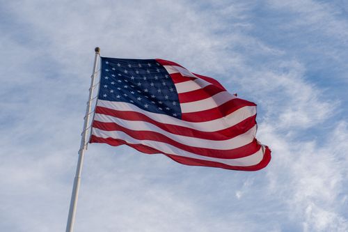 Free A vibrant American flag waves against a clear blue sky symbolizing freedom and patriotism. Stock Photo
