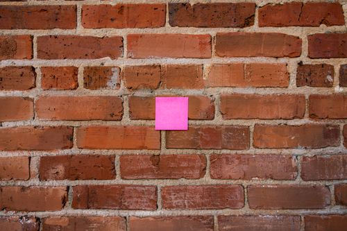Free A vibrant pink sticky note posted on a textured red brick wall, showcasing contrasts. Stock Photo
