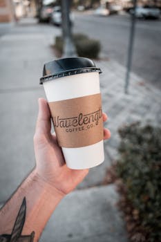 Close-up of a hand holding a Wavelength Coffee disposable cup outdoors on a city street.
