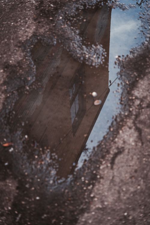 Free Reflection of a building in a puddle on a city street, capturing urban life creatively. Stock Photo