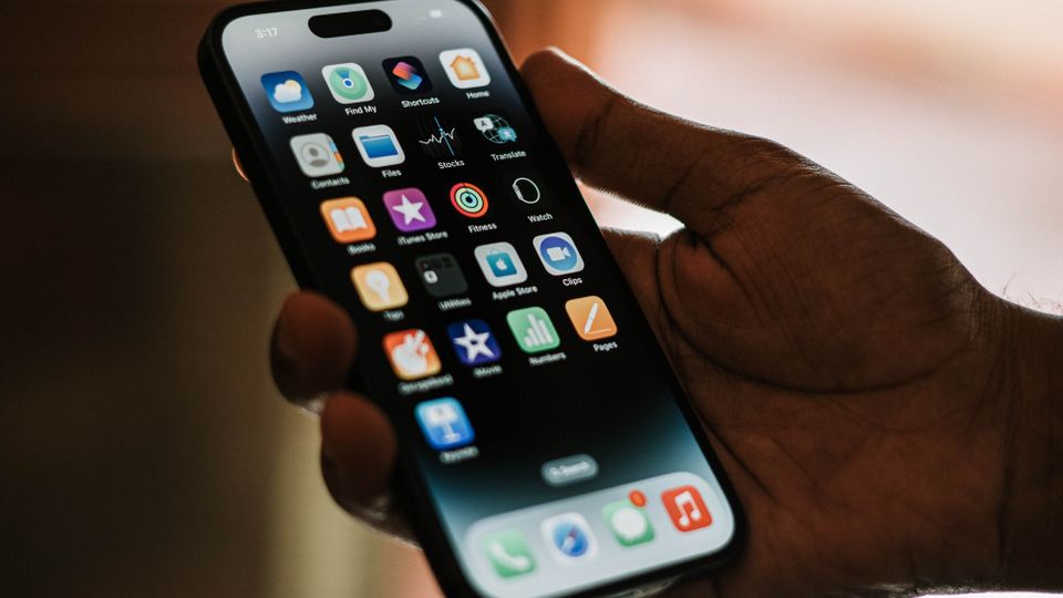 Mão segurando um smartphone com ícones de aplicativos na tela, representando o uso de apps mobile.