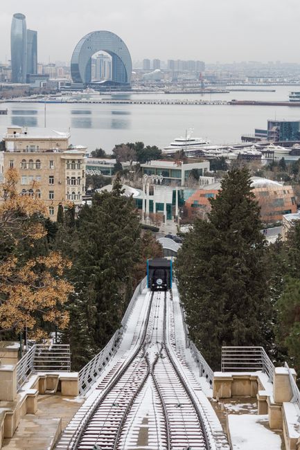 A snowy winter cityscape featuring a cable car and modern architecture by the Caspian Sea in Baku.