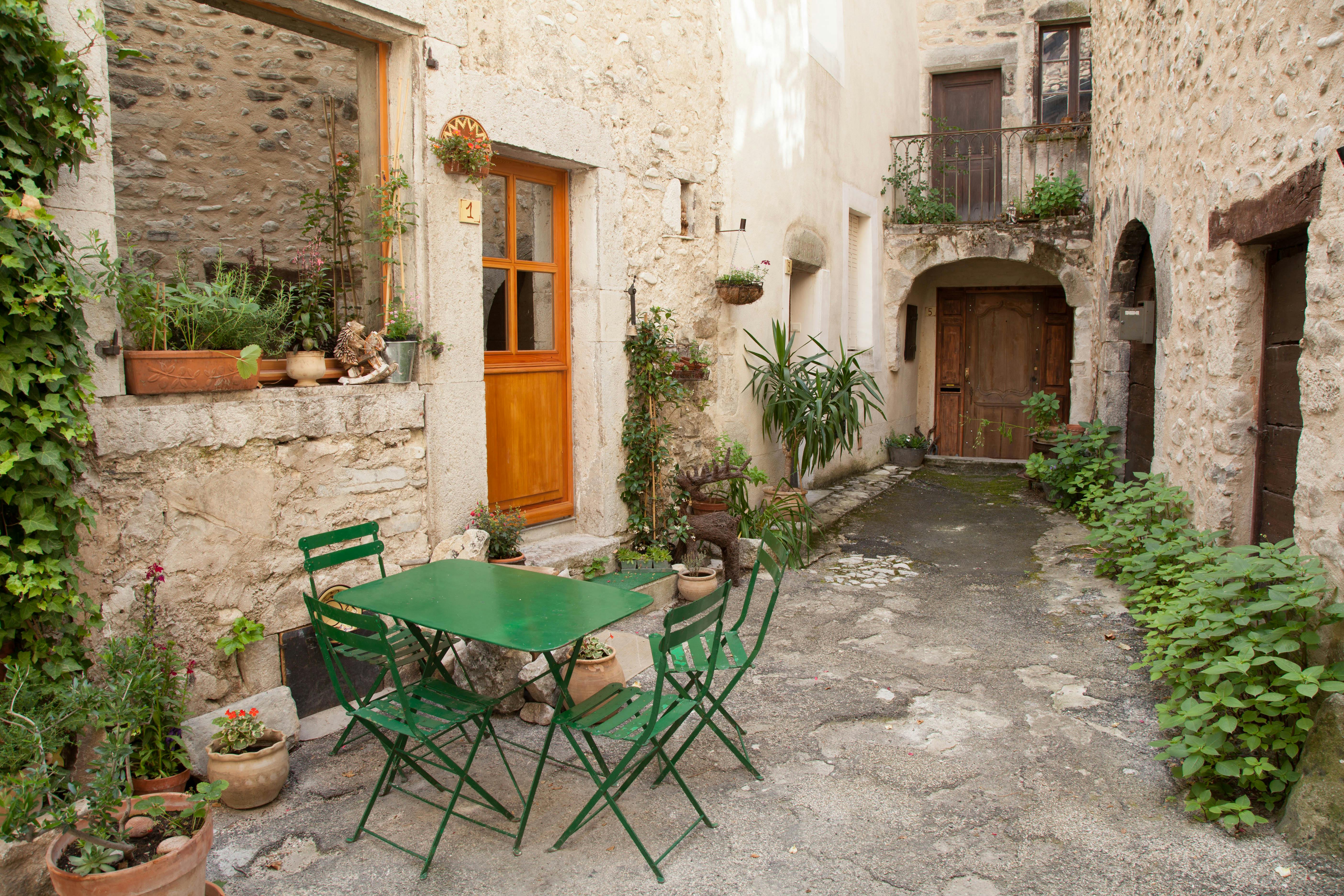Quaint stone alley in Die, France featuring green tables and chairs surrounded by lush plants.