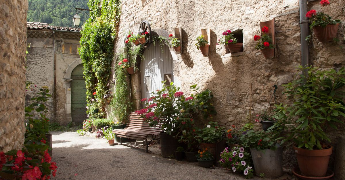 A narrow cobblestone alley with colorful flowers hanging from stone walls in a remote European village