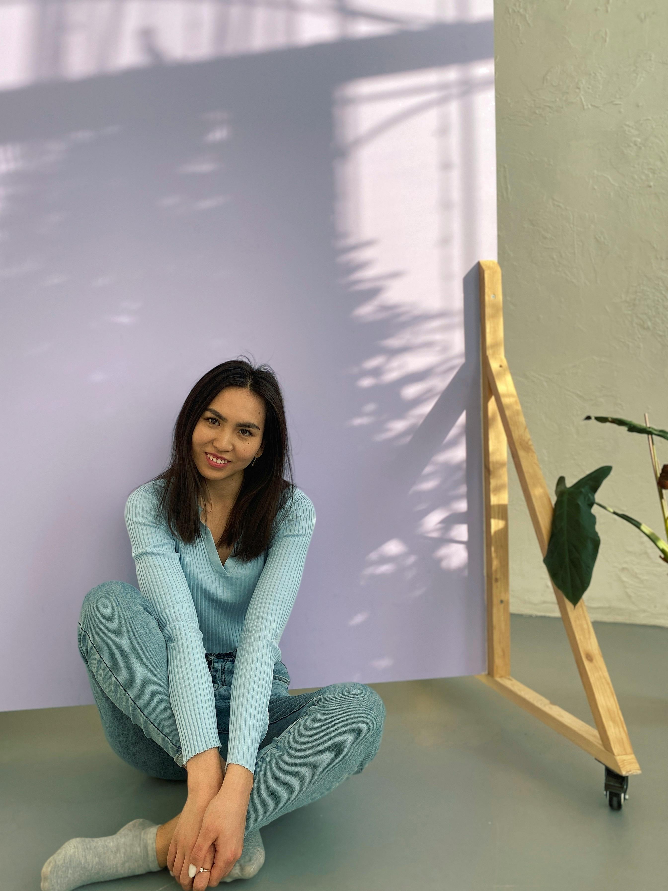Woman in jeans and sweater sitting cross-legged on studio floor.