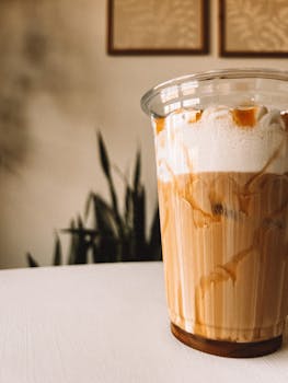 Close-up of a delicious iced caramel macchiato in a plastic cup with cream, perfect for a refreshing caffeine fix.