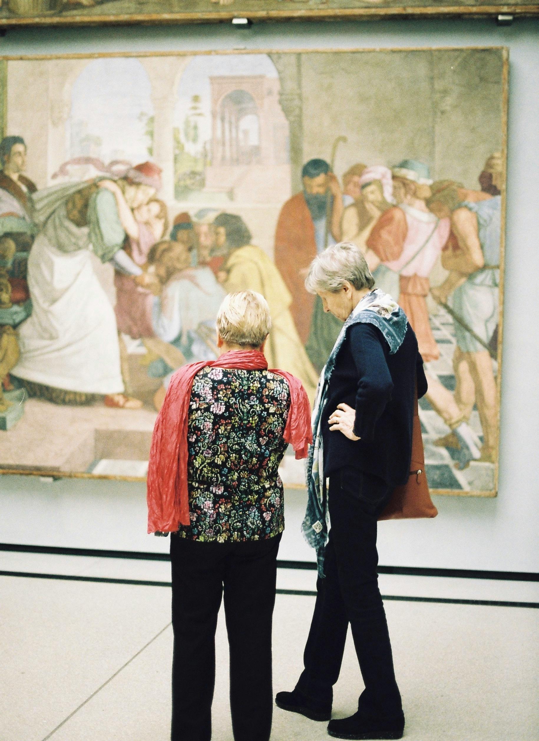 Senior women viewing a historical painting in an art gallery, appreciating culture.