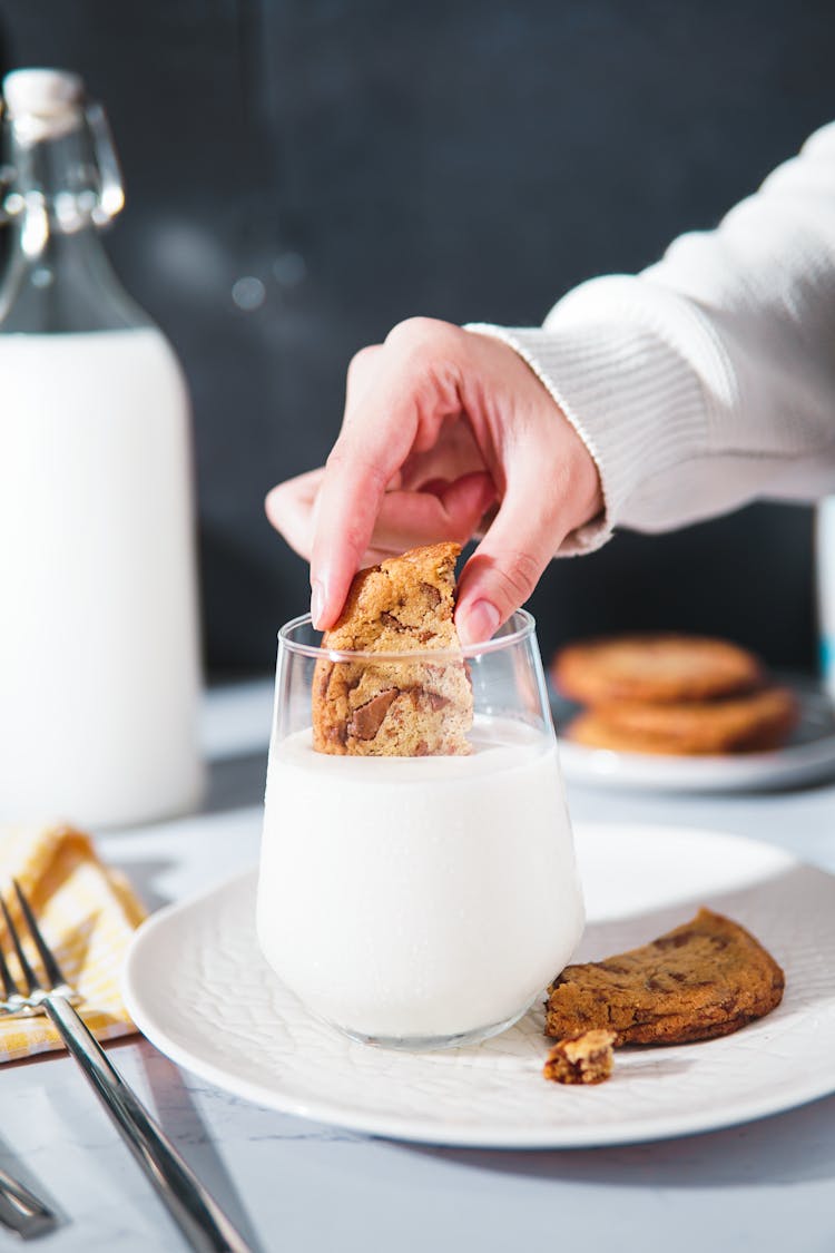 Person Dipping Cookie In Glass Filled With Milk