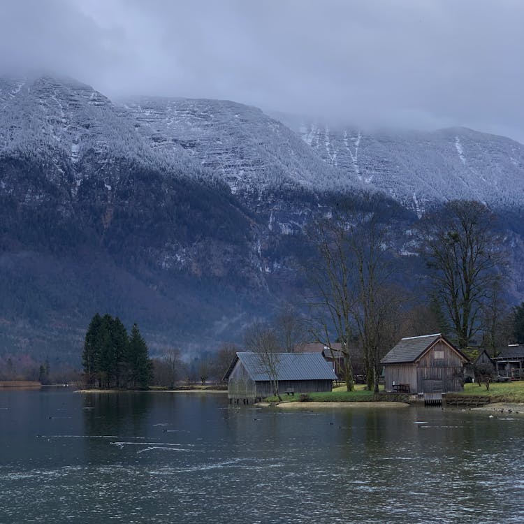 Wooden Cabins On River Bank In Mountains Landscape