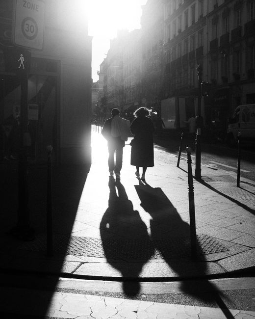 Silhouetted couple walking down a Paris street in dramatic black and white.