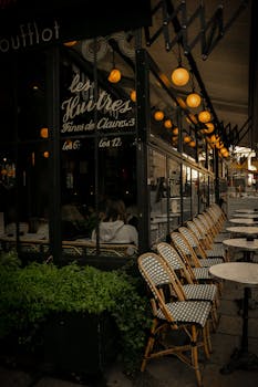 Elegant outdoor seating at a Parisian cafe with illuminated lights and classic wicker chairs.