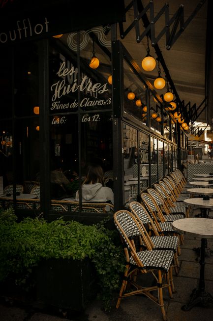 Elegant outdoor seating at a Parisian cafe with illuminated lights and classic wicker chairs.