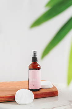 Elegant skincare bottle on a wooden board with cotton pads and green leaves