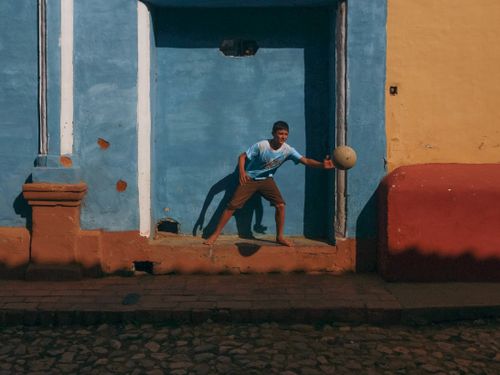 Free A young boy plays with a ball against a vibrant blue wall on a sunny day. Stock Photo