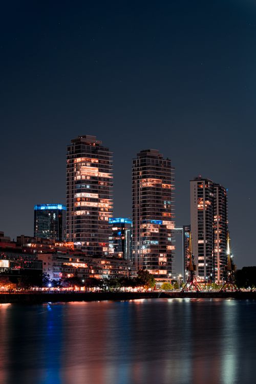 Free Stunning nighttime cityscape with skyscrapers reflecting on a calm river, showcasing urban beauty. Stock Photo