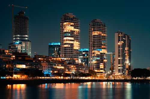 Free Night view of a vibrant urban skyline with skyscrapers reflecting on a river. Stock Photo