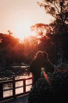 A couple enjoys a serene sunset by a lakeside in a peaceful park setting.
